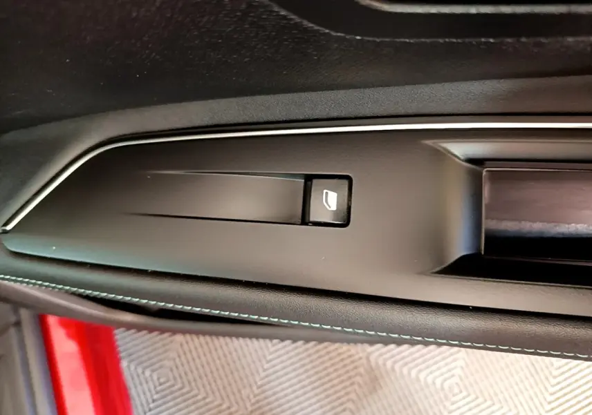 Détail de la poignée intérieure noire avec bouton d’ouverture sur la porte côté conducteur d’un Peugeot 3008 rouge.