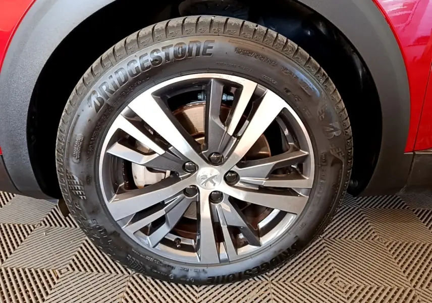 Gros plan sur la roue avant droite du Peugeot 3008 hybride rouge, avec jante alliage gris et pneu Bridgestone.