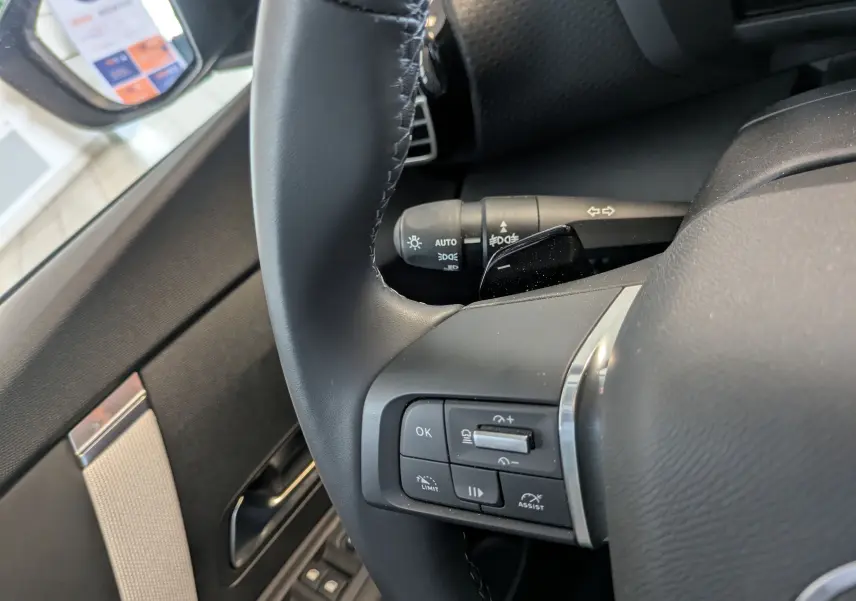 Gros plan sur le volant noir côté gauche de la Citroën C4 1.2 Hybride 2025 avec commandes intégrées et partie de la portière visible.