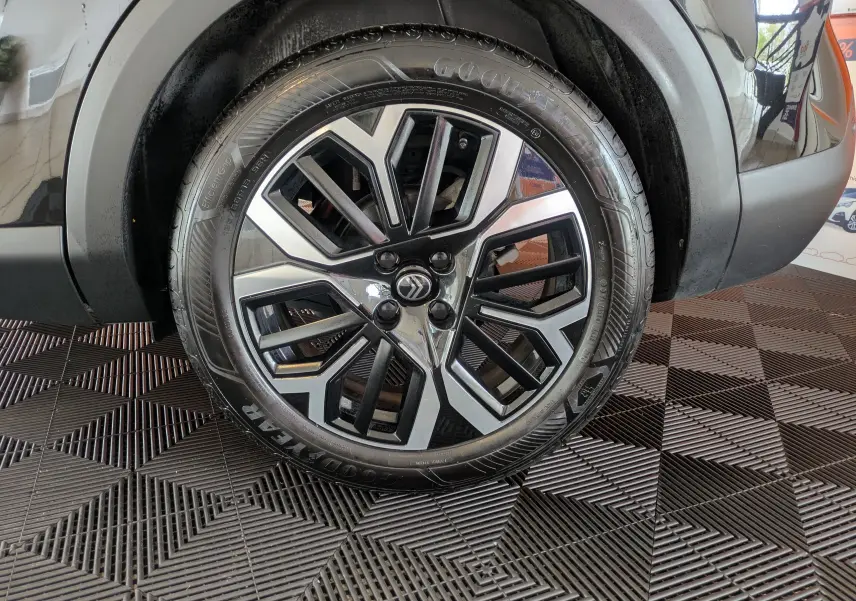 Gros plan sur la roue avant droite noire d'une Citroën C4 1.2 Hybride 136ch avec jante alliage bicolore design.