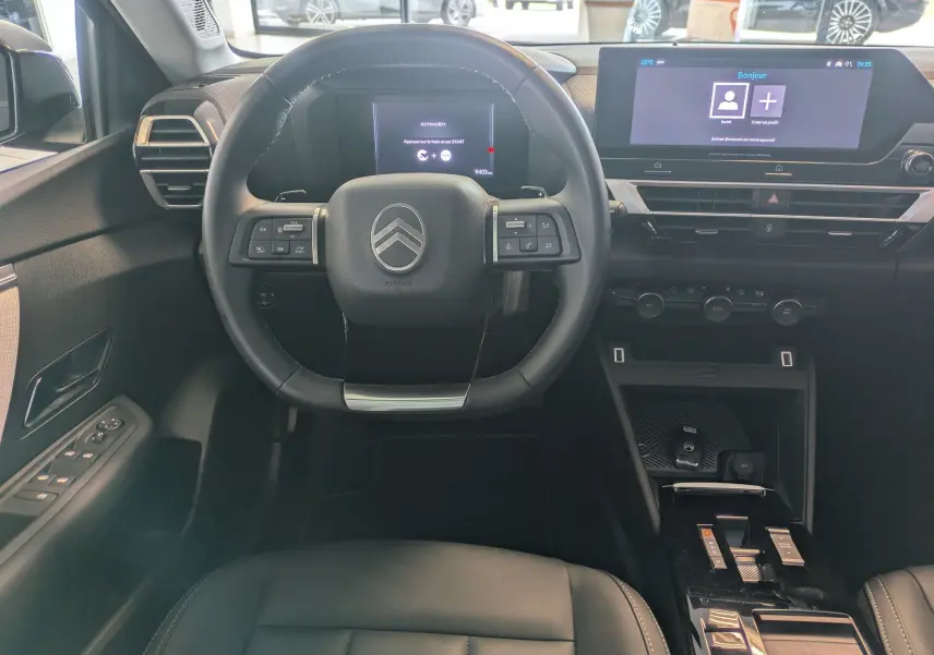 Vue intérieure centrée sur le volant et tableau de bord noir de la Citroën C4 hybride avec écran tactile et commandes au volant.