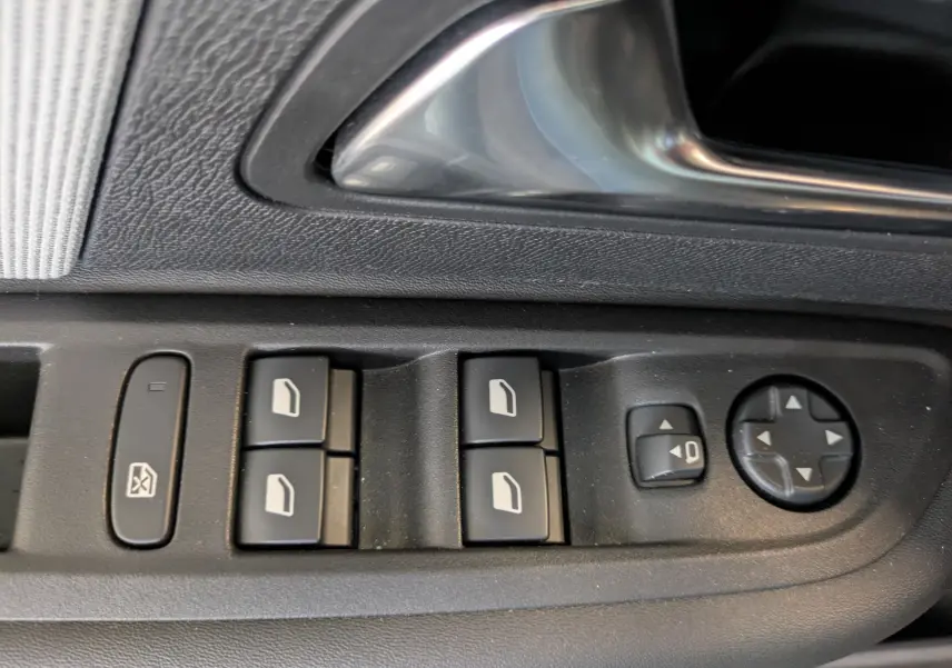 Gros plan sur les commandes des vitres électriques et réglages des rétroviseurs côté conducteur d'une Citroën C4 noire.