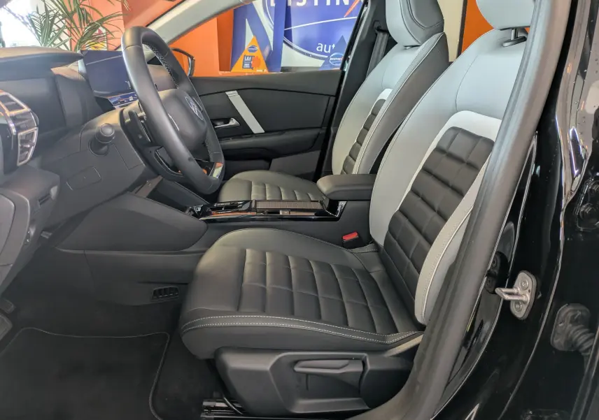 Vue intérieure côté conducteur de la Citroën C4 noire 2025, sièges bi-ton cuir noir et gris avec console centrale brillante.
