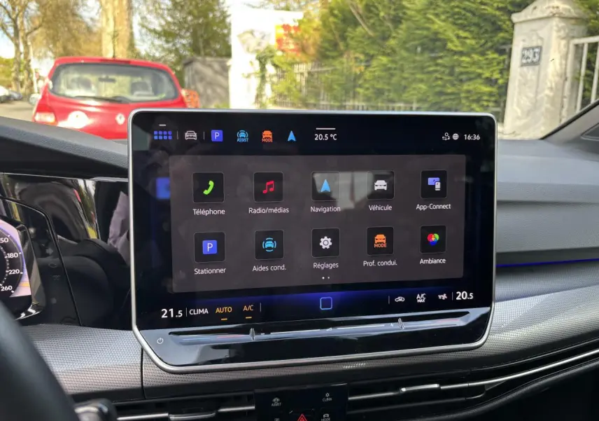 Vue intérieure du tableau de bord de la Volkswagen Golf 2024 blanc, avec écran tactile central affichant les options multimédia et navigation.