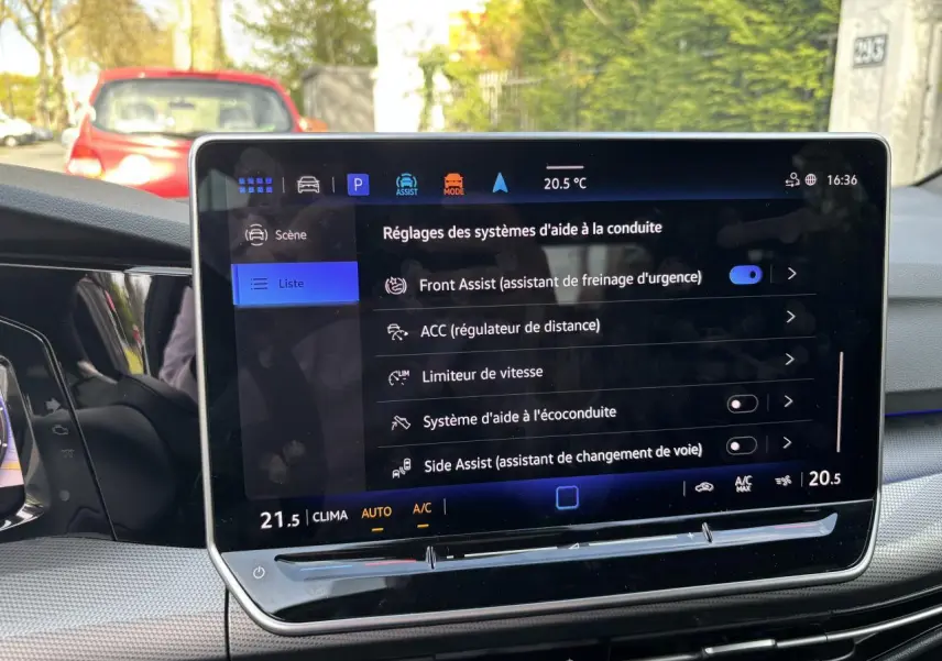 Vue intérieure du tableau de bord de la Volkswagen Golf blanche 2024, écran tactile affichant les aides à la conduite.
