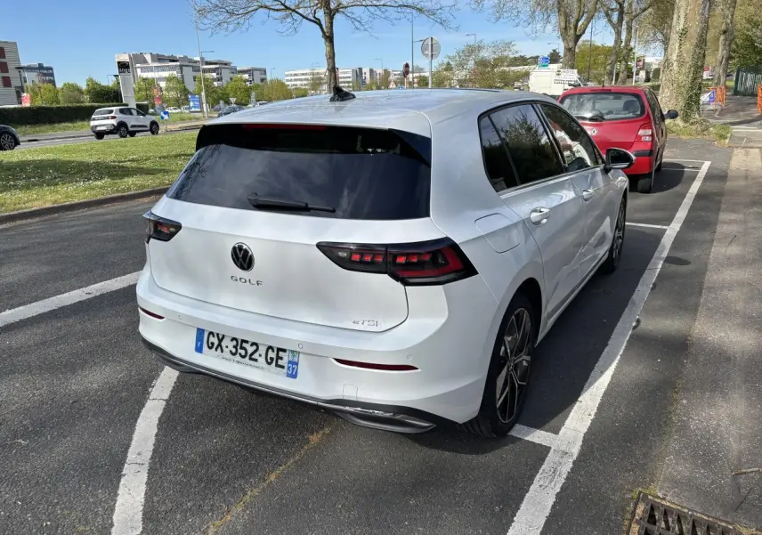 Vue 3/4 arrière droite d'une Volkswagen Golf blanche 2024, avec feux arrière LED et vitres teintées, stationnée sur rue.