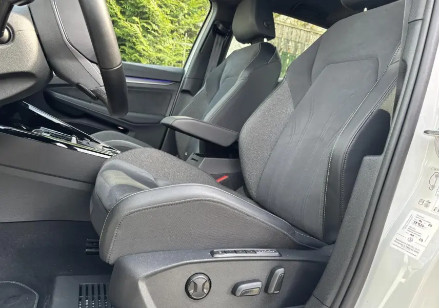 Vue intérieure côté conducteur de la Volkswagen Golf blanche 2024, mettant en valeur le siège avant en tissu et cuir avec réglages électriques.