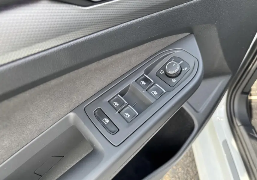 Vue rapprochée des commandes des vitres et des rétroviseurs sur la porte côté gauche d'une Volkswagen Golf blanche 2024.