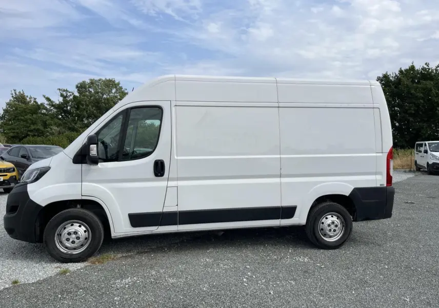Vue de profil côté gauche d’un Peugeot Boxer Fourgon blanc avec porte latérale coulissante tôlée sur un parking extérieur.