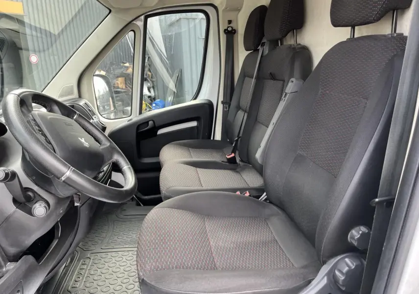 Vue intérieure côté conducteur du Peugeot Boxer Fourgon 2023, sièges tissu noir avec motifs rouges et volant cuir.