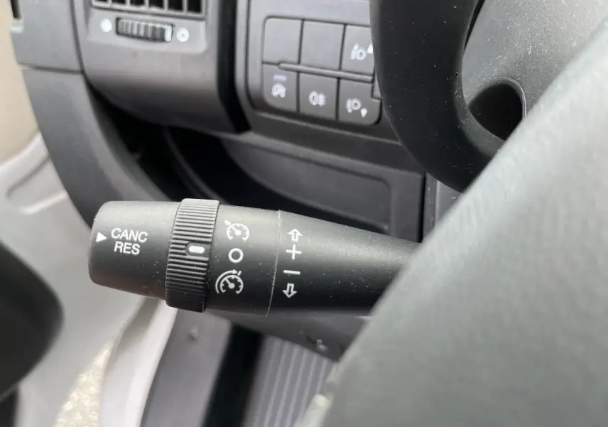 Gros plan sur la commande de régulateur de vitesse à gauche du volant dans l'habitacle du Peugeot Boxer blanc.