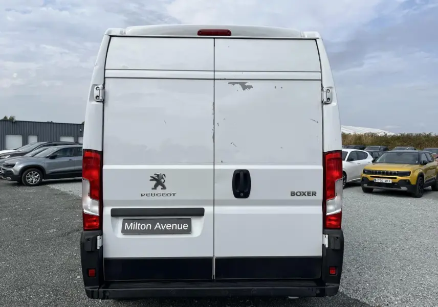 Vue arrière d'un Peugeot Boxer Fourgon blanc avec portes tôlées et logo Peugeot visible, stationné sur un parking.
