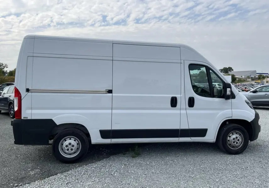 Vue latérale droite d’un Peugeot Boxer Fourgon blanc 2023 avec porte coulissante tôlée et protections noires.