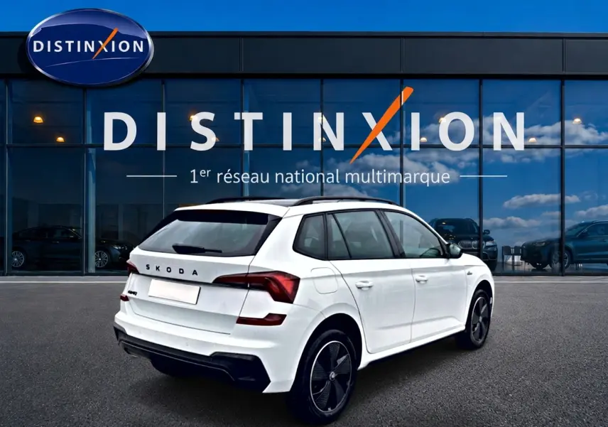 Vue 3/4 arrière droite d'un Skoda Kamiq blanc nacré avec jantes alu noires, devant une vitrine Distinxion.