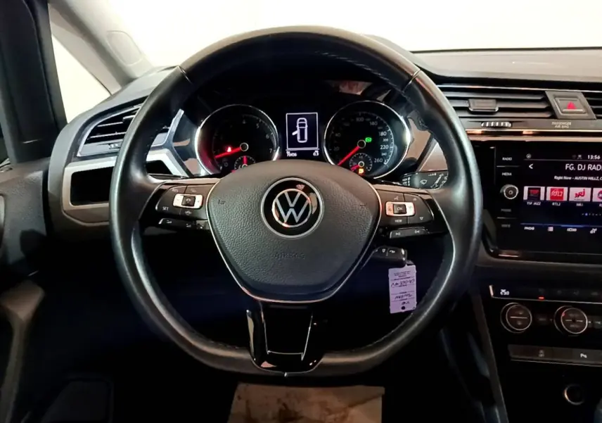 Volant cuir noir vu de face dans l'habitacle d'un Volkswagen Touran bleu, avec écran tactile et commandes au volant.
