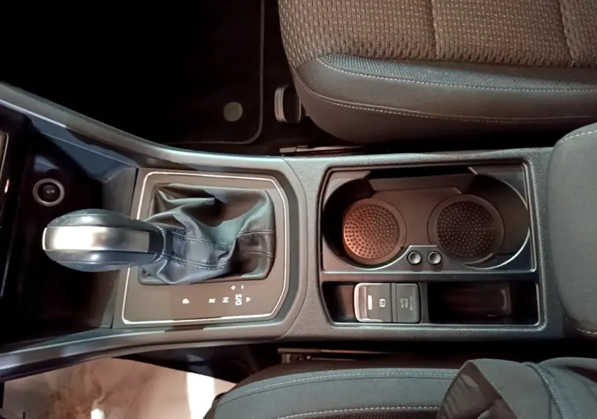 Vue plongeante sur la console centrale noire du Volkswagen Touran 1.5 TSI EVO DSG7 United avec levier de vitesse automatique et porte-gobelets.