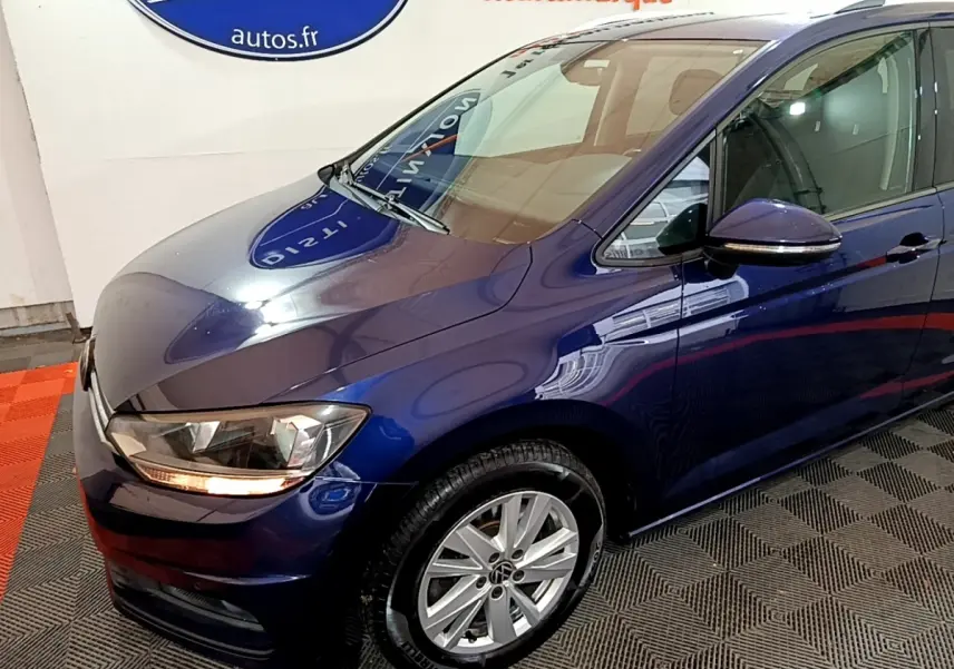 Vue 3/4 avant gauche d'un Volkswagen Touran bleu 2021 avec phares allumés et jantes alliage argentées.