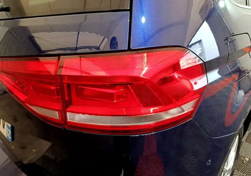 Gros plan sur le feu arrière gauche rouge d’un Volkswagen Touran bleu 2021, avec reflet intérieur visible.