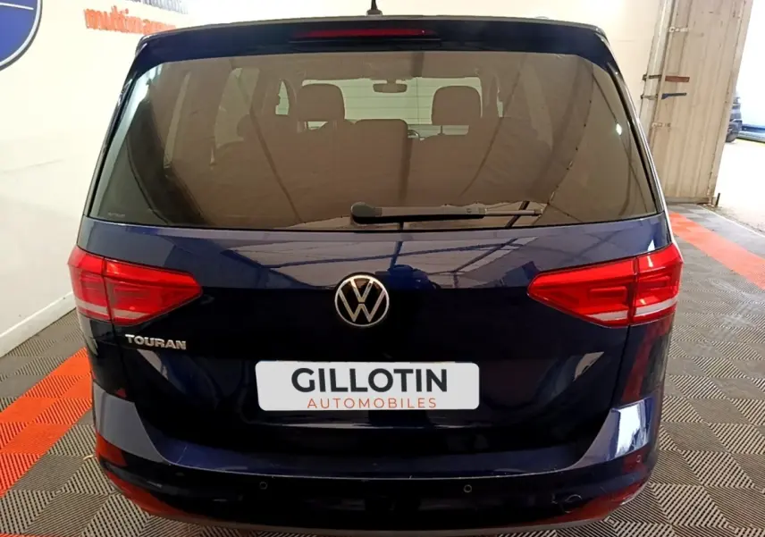 Vue arrière d'un Volkswagen Touran bleu foncé garé en intérieur avec logo et feux rouges visibles.