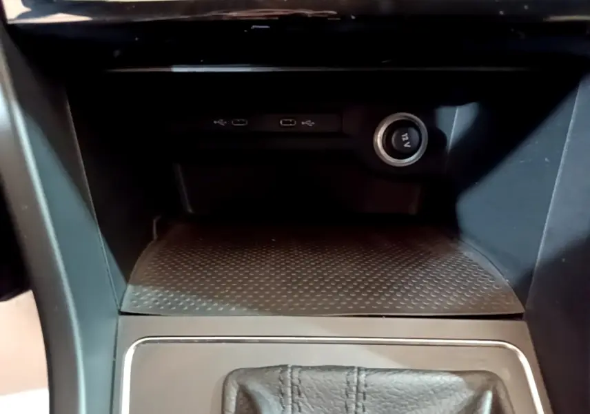 Gros plan sur la console centrale noire du Volkswagen Touran 1.5 TSI EVO DSG7 avec prise 12V et ports USB visibles.