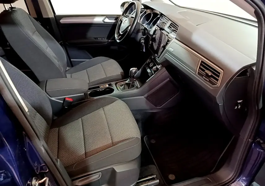 Intérieur avant du Volkswagen Touran bleu 2021, vue côté conducteur, tableau de bord moderne avec écran tactile central.