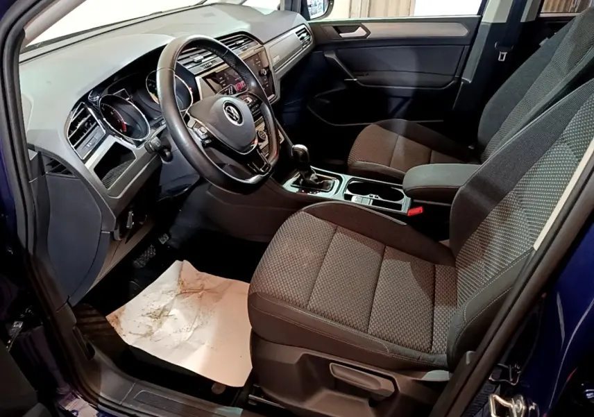 Vue intérieure côté conducteur du Volkswagen Touran bleu 2021, montrant le volant cuir multifonctions et les sièges tissu gris.