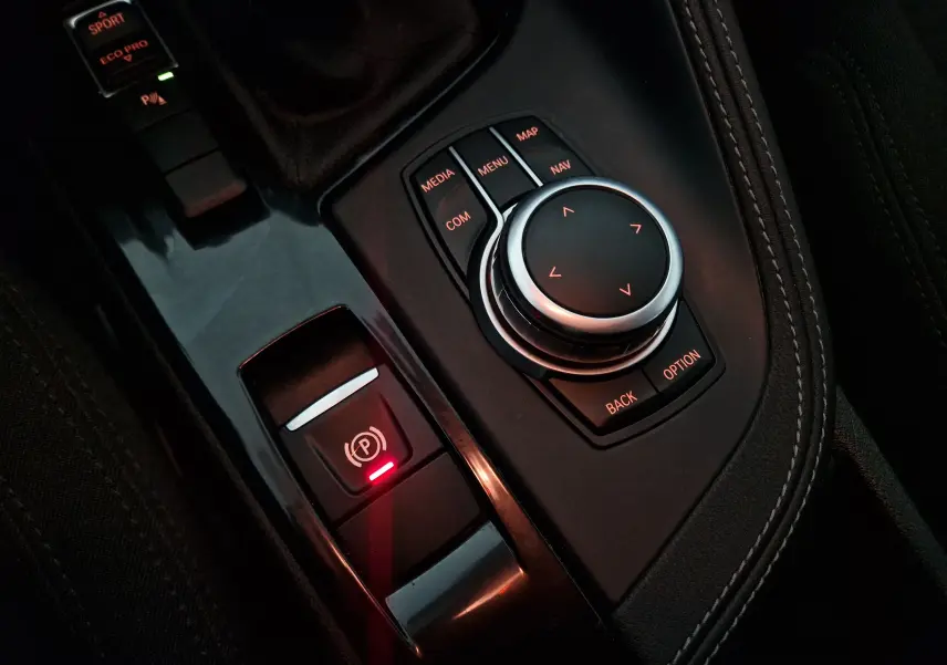 Gros plan sur la molette de commande multimédia et le frein à main électrique du BMW X2 gris clair, intérieur noir.