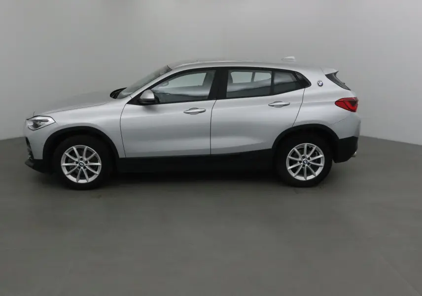 BMW X2 gris clair métal vue de profil côté gauche dans un studio, soulignant ses lignes compactes et ses jantes alliage.