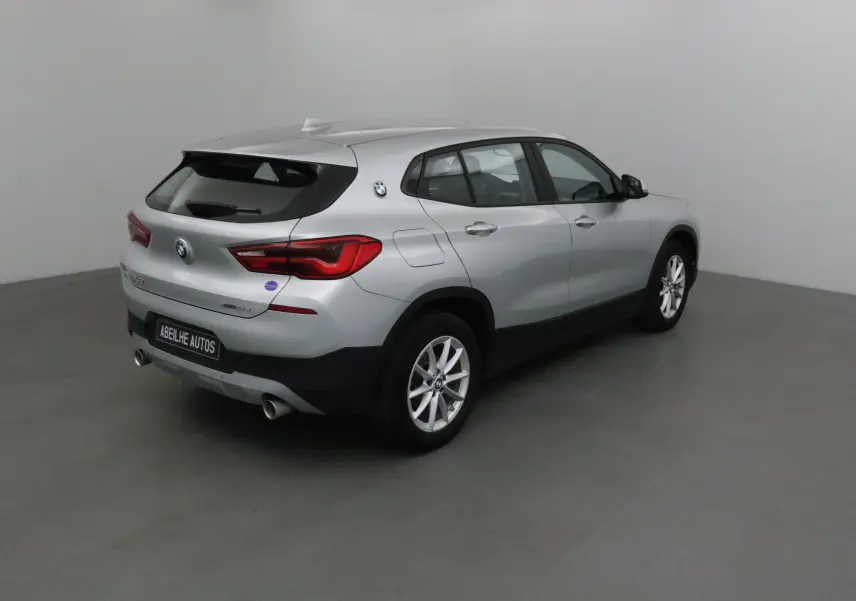 BMW X2 gris clair métal vue 3/4 arrière droit, avec jantes alliage et double sortie d’échappement.
