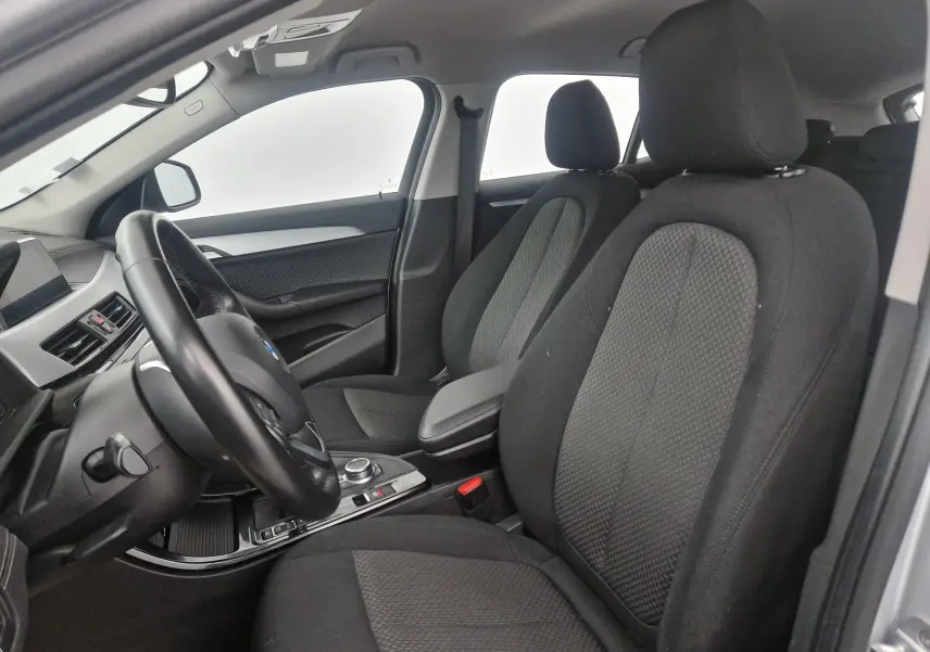 Vue intérieure côté conducteur de la BMW X2 gris clair métal, montrant les sièges avant en tissu noir et la console centrale.