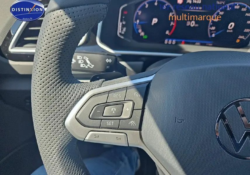 Gros plan sur le volant cuir perforé côté gauche du Volkswagen T-Roc noir perle avec commandes multifonctions et cockpit numérique en arrière-plan.