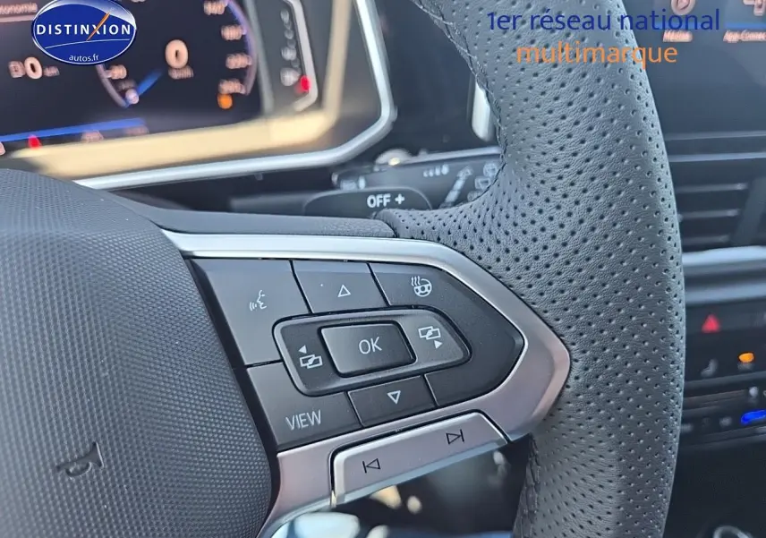 Gros plan sur le volant cuir perforé du Volkswagen T-Roc noir perle, avec commandes multifonctions et cockpit numérique en arrière-plan.