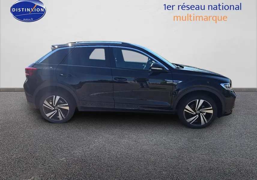Profil côté gauche du Volkswagen T-Roc noir perle 2025 avec jantes alliage et barres de toit argentées.