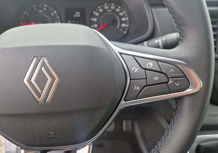 Gros plan sur le volant noir du Renault Trafic Fourgon 2025 avec commandes intégrées et logo Renault central.