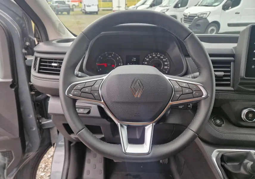Vue intérieure centrée sur le volant noir du Renault Trafic Fourgon gris Highland avec tableau de bord et commandes visibles.