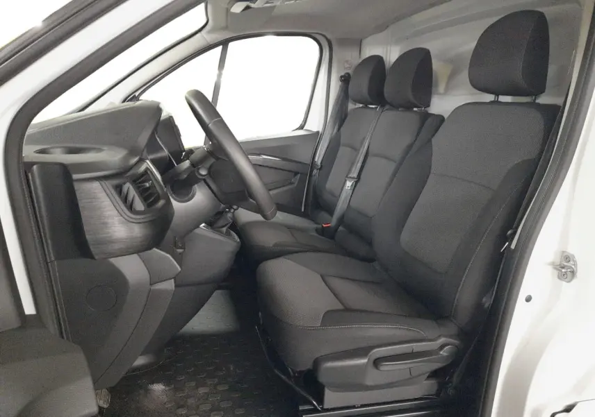 Vue intérieure côté conducteur du Renault Trafic Fourgon blanc 2024, montrant le tableau de bord et les sièges tissu noir et gris.