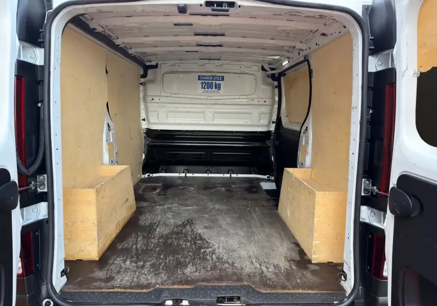Vue intérieure arrière du fourgon blanc Renault Trafic L1H1 2024, avec aménagements en bois sur les côtés et plancher usé.