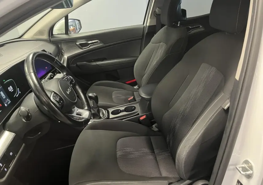 Intérieur avant du Kia Sportage blanc 2022, vue côté conducteur avec sièges noirs et volant cuir multifonction.