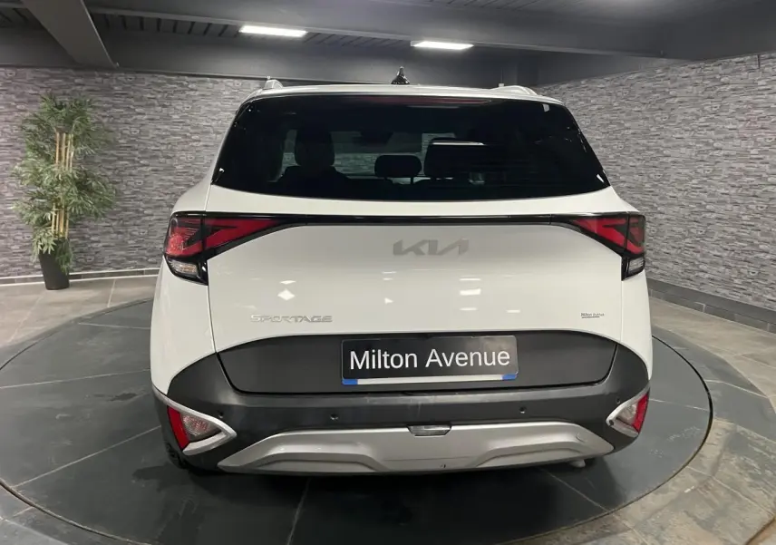 Vue arrière d'un KIA Sportage blanc nacré avec bouclier noir laqué et feux arrière LED en intérieur showroom.