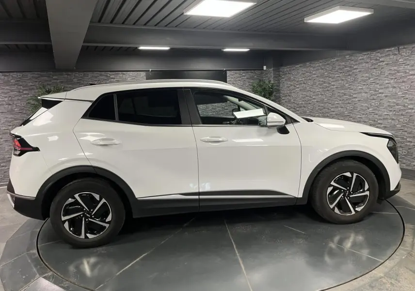 Vue latérale droite d’un KIA Sportage blanc nacré avec jantes alliage 18 pouces et vitres surteintées.