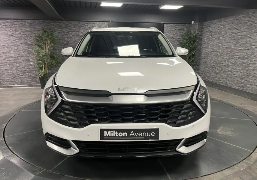 Vue avant d'un KIA SPORTAGE blanc nacré avec calandre noire laquée et feux LED en forme de boomerang.