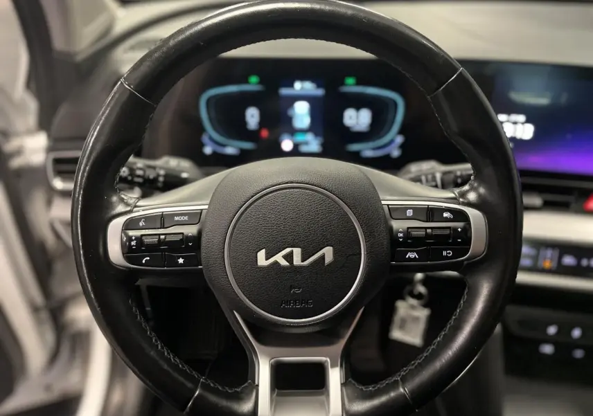 Gros plan sur le volant cuir noir du Kia Sportage 2022 avec commandes intégrées et tableau de bord digital flou en arrière-plan.