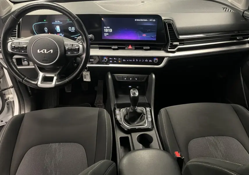 Vue intérieure avant du Kia Sportage 2022 blanc, avec tableau de bord digital et levier de vitesse manuel central.