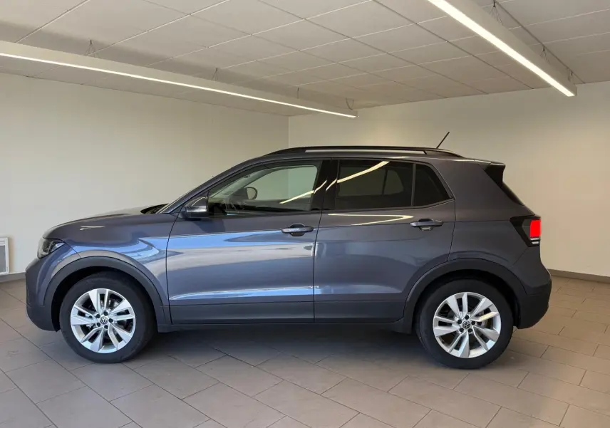 Profil côté gauche du Volkswagen T-Cross gris cendre 2025 en version 1.0 TSI 116 BVM6 VW EDITION, intérieur showroom.