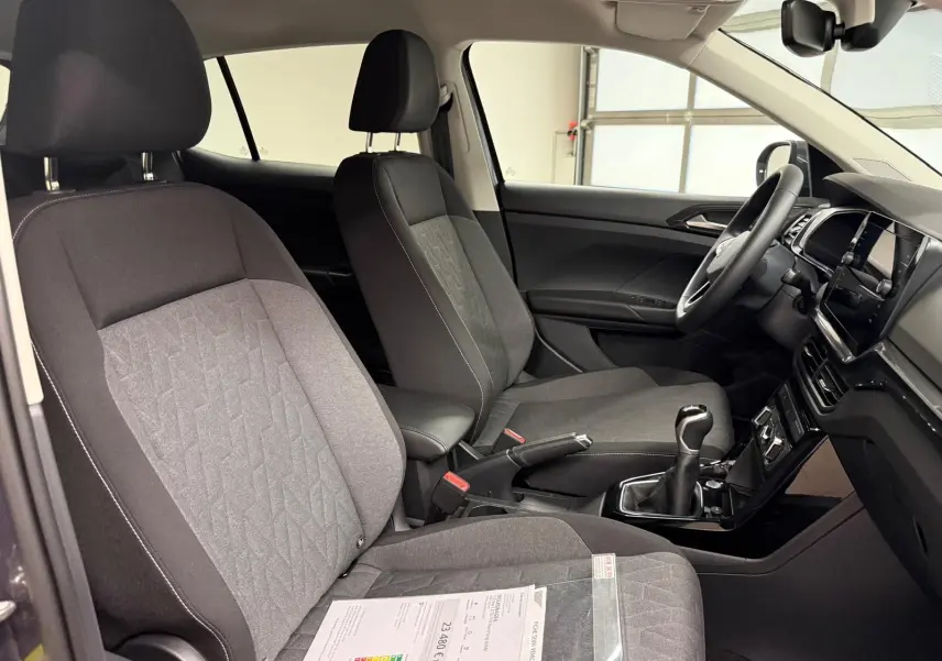Vue intérieure côté conducteur du Volkswagen T-Cross gris cendre 2025, montrant les sièges tissu et la boîte manuelle.
