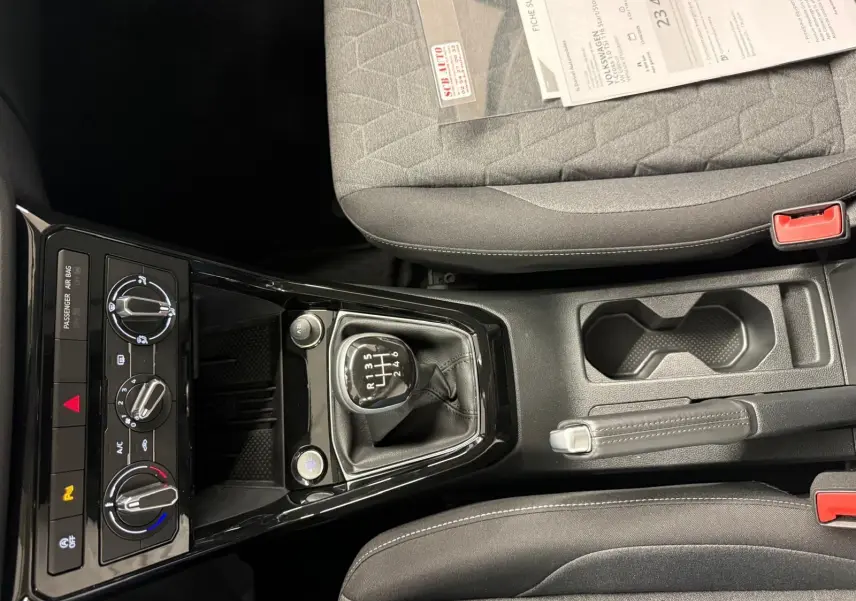 Vue intérieure centrée sur la console centrale du Volkswagen T-Cross gris cendre, avec levier de vitesse manuel et commandes climatisation.