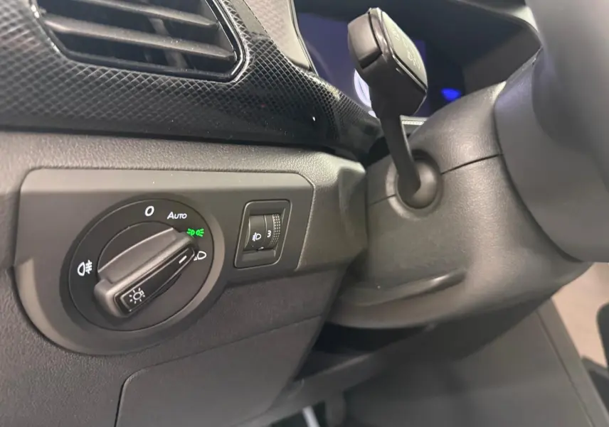 Détail du tableau de bord côté gauche du Volkswagen T-Cross gris cendre 2025, avec commande des phares et régulateur de hauteur.