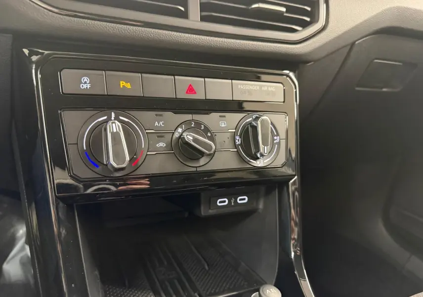 Gros plan sur la console centrale du Volkswagen T-Cross 2025, avec commandes climatisation et ports USB visibles.