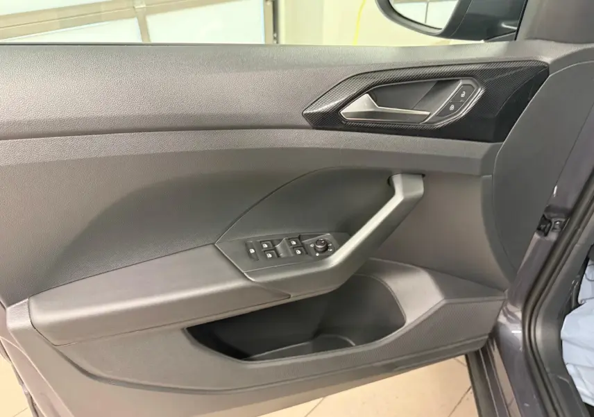 Vue intérieure de la porte avant gauche du Volkswagen T-Cross gris cendre, avec commandes des vitres et poignée intégrée.