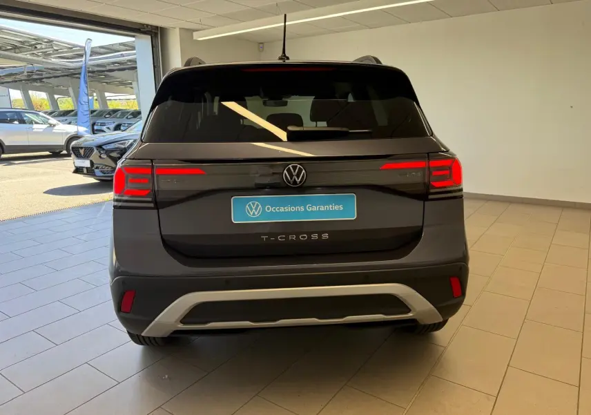 Vue arrière d'un Volkswagen T-Cross gris cendre 2025 avec feux arrière allumés et logo VW visible.